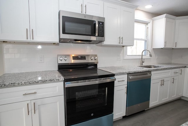 kitchen featuring tasteful backsplash, light stone counters, stainless steel appliances, white cabinetry, and a sink