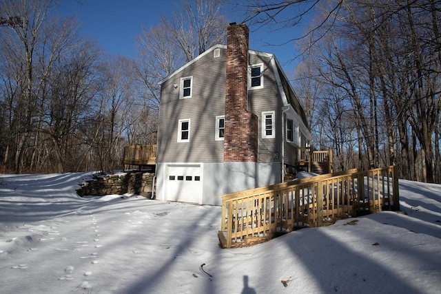 view of snow covered exterior featuring a garage, a chimney, and a wooden deck