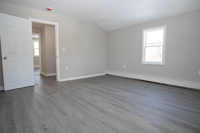 unfurnished room featuring a baseboard radiator, lofted ceiling, baseboards, and wood finished floors