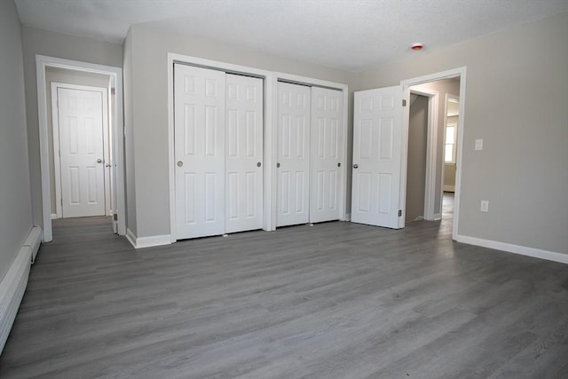 unfurnished bedroom featuring dark wood-type flooring, baseboards, baseboard heating, and multiple closets