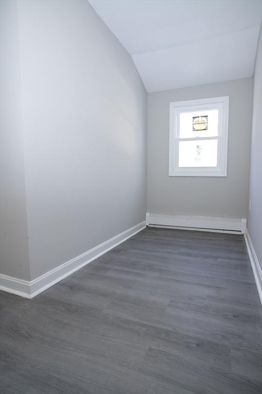 unfurnished room with vaulted ceiling, baseboards, baseboard heating, and dark wood finished floors