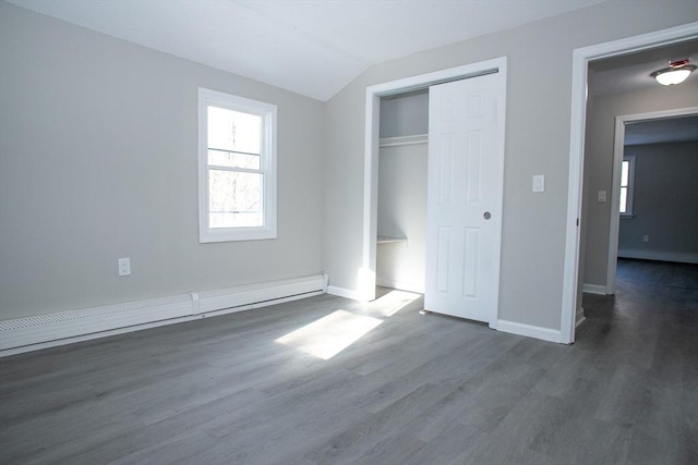 unfurnished bedroom featuring lofted ceiling, a closet, a baseboard heating unit, wood finished floors, and baseboards