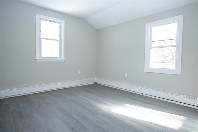 additional living space featuring a healthy amount of sunlight, a baseboard heating unit, vaulted ceiling, and wood finished floors