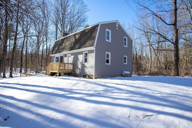 exterior space with a shingled roof, a chimney, a wooden deck, and a gambrel roof