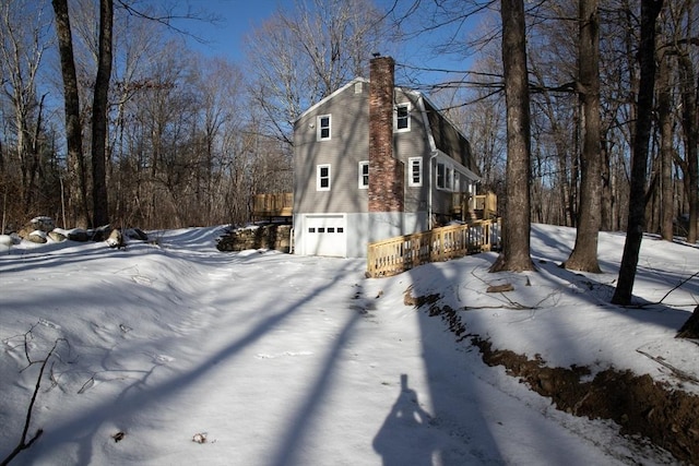 snow covered property featuring a garage and a chimney