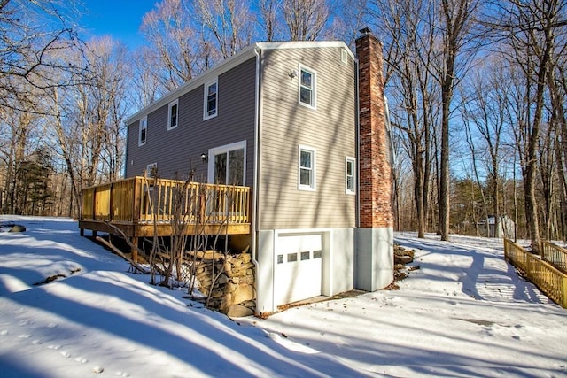 view of snow covered exterior with a deck, a chimney, and a garage