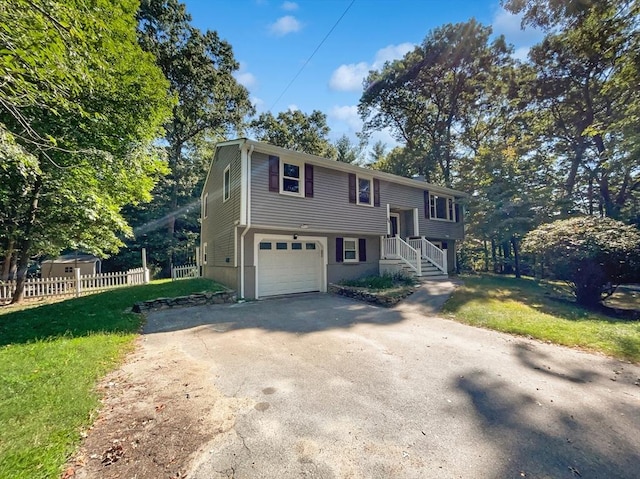 bi-level home featuring an attached garage, aphalt driveway, a front yard, and fence