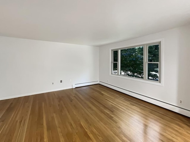 empty room featuring a baseboard heating unit, baseboards, and wood finished floors