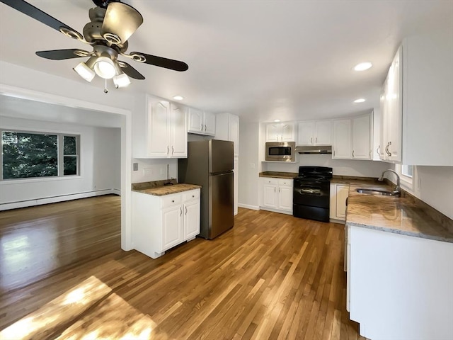 kitchen with under cabinet range hood, a baseboard heating unit, a sink, light wood-style floors, and appliances with stainless steel finishes