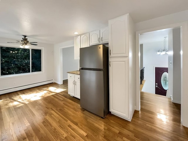 kitchen featuring light wood-style flooring, a baseboard heating unit, freestanding refrigerator, white cabinets, and ceiling fan with notable chandelier