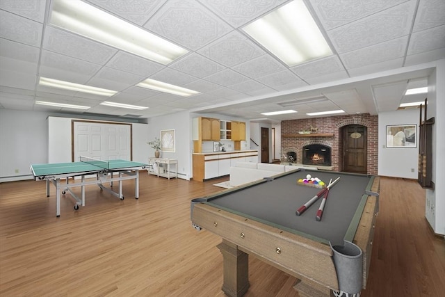 recreation room featuring a paneled ceiling, a fireplace, pool table, and light hardwood / wood-style flooring