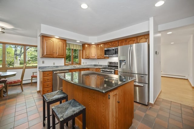 kitchen with stainless steel appliances, light tile patterned floors, a baseboard heating unit, a kitchen bar, and a kitchen island