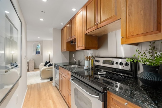 kitchen featuring light wood finished floors, appliances with stainless steel finishes, brown cabinets, dark stone countertops, and a sink