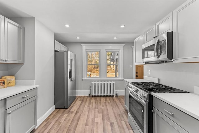 kitchen with gray cabinets, appliances with stainless steel finishes, radiator, and light wood-type flooring