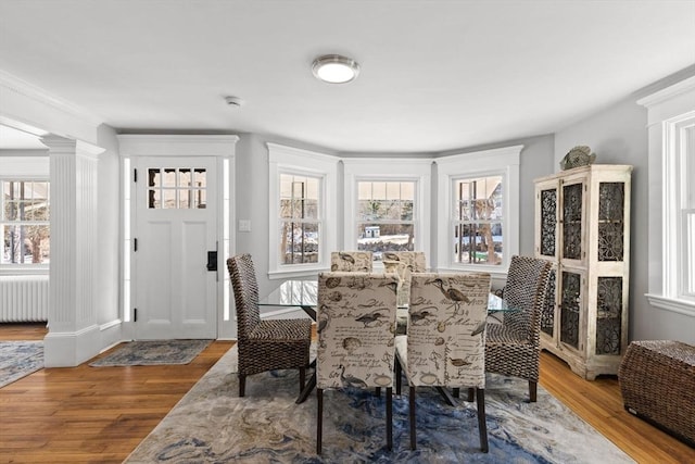 dining room with radiator heating unit, wood-type flooring, and ornate columns