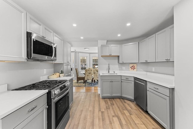 kitchen with gray cabinets, appliances with stainless steel finishes, sink, and light hardwood / wood-style flooring