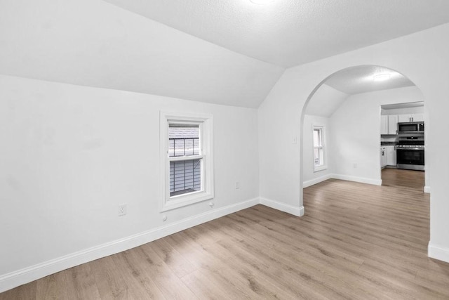 interior space with light wood-type flooring, lofted ceiling, and a textured ceiling