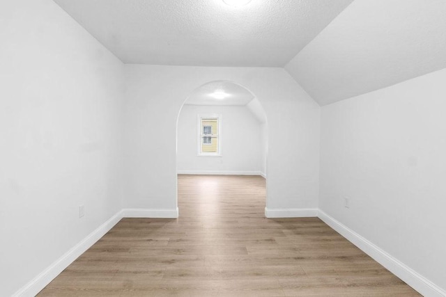 additional living space featuring a textured ceiling, vaulted ceiling, and light wood-type flooring