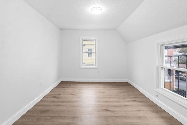 additional living space with a textured ceiling, plenty of natural light, light hardwood / wood-style floors, and lofted ceiling