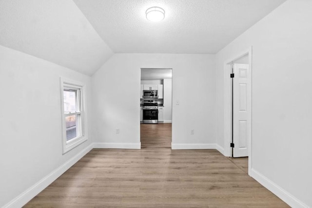 interior space featuring a textured ceiling, light hardwood / wood-style flooring, and lofted ceiling