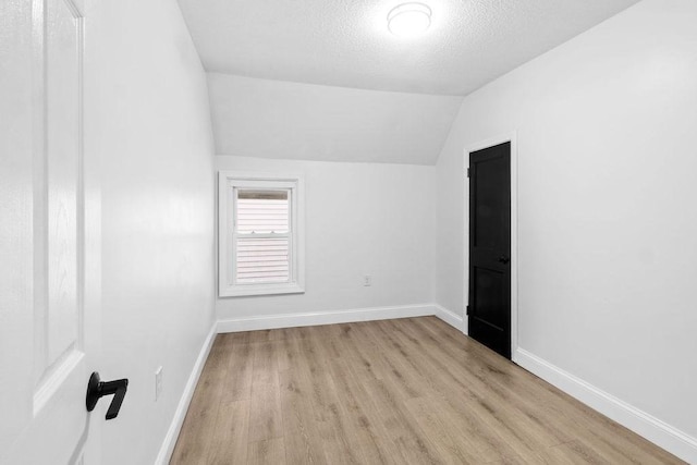 empty room with light hardwood / wood-style floors, a textured ceiling, and vaulted ceiling