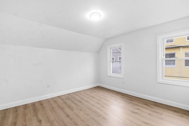 bonus room with a healthy amount of sunlight, lofted ceiling, a textured ceiling, and light hardwood / wood-style flooring