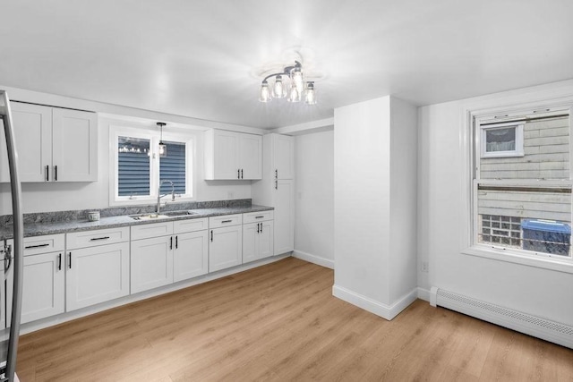 kitchen with white cabinets, sink, light hardwood / wood-style flooring, baseboard heating, and a notable chandelier