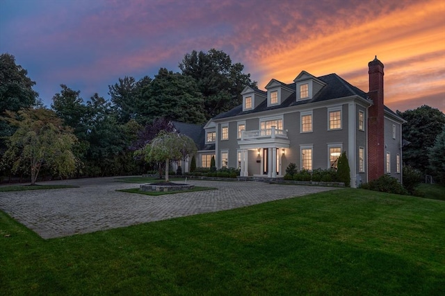 view of front of house with a chimney, decorative driveway, a lawn, and a balcony