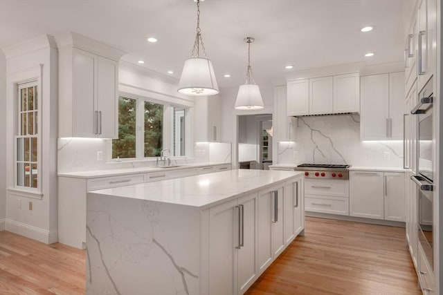 kitchen with light wood finished floors, a center island, stainless steel gas stovetop, white cabinetry, and a sink