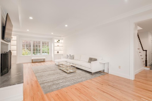 living room with a fireplace with raised hearth, recessed lighting, wood finished floors, built in features, and stairway