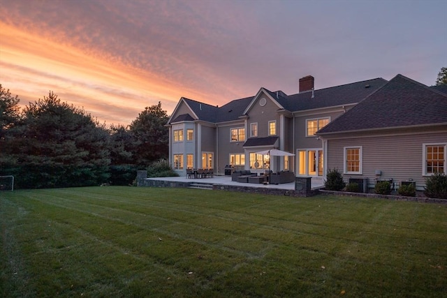 back of property at dusk with a yard, a chimney, and a patio