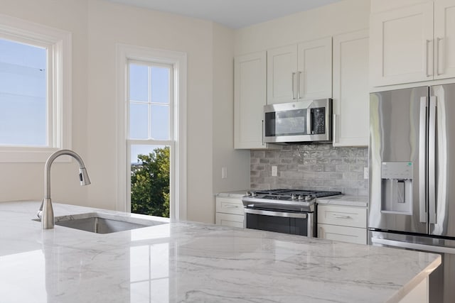 kitchen with a wealth of natural light, decorative backsplash, white cabinets, and appliances with stainless steel finishes