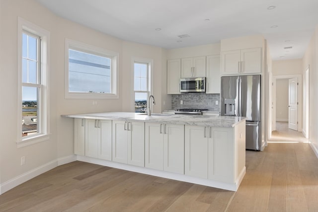 kitchen featuring a sink, light wood-style floors, appliances with stainless steel finishes, a peninsula, and decorative backsplash