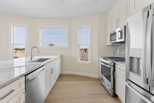 kitchen with light stone countertops, sink, light hardwood / wood-style floors, white cabinets, and appliances with stainless steel finishes