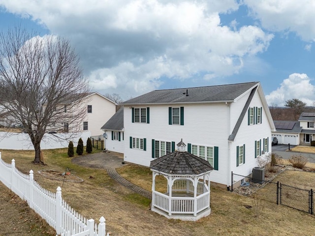 rear view of property with a gazebo, a yard, central AC, and a fenced backyard