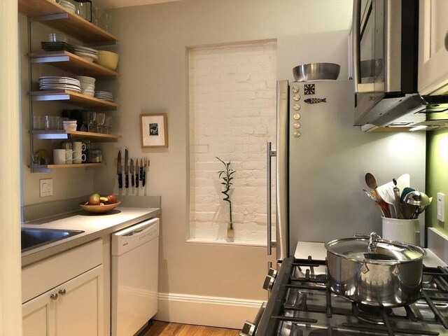 kitchen with open shelves, a sink, dishwasher, stainless steel microwave, and wood finished floors