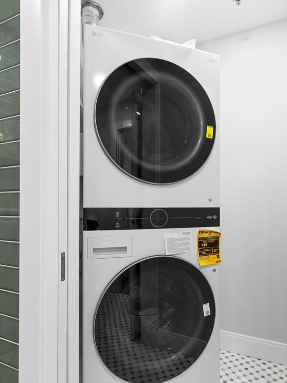 laundry room featuring stacked washing maching and dryer, laundry area, baseboards, and tile patterned floors