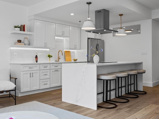 kitchen featuring island exhaust hood, freestanding refrigerator, a kitchen breakfast bar, white cabinetry, and backsplash