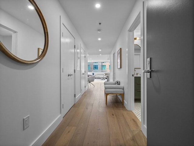 hallway featuring light wood finished floors, baseboards, and recessed lighting