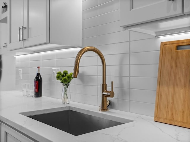 details with white cabinetry, decorative backsplash, light stone countertops, and a sink