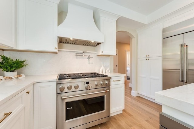 kitchen with arched walkways, light stone counters, premium appliances, custom range hood, and white cabinetry