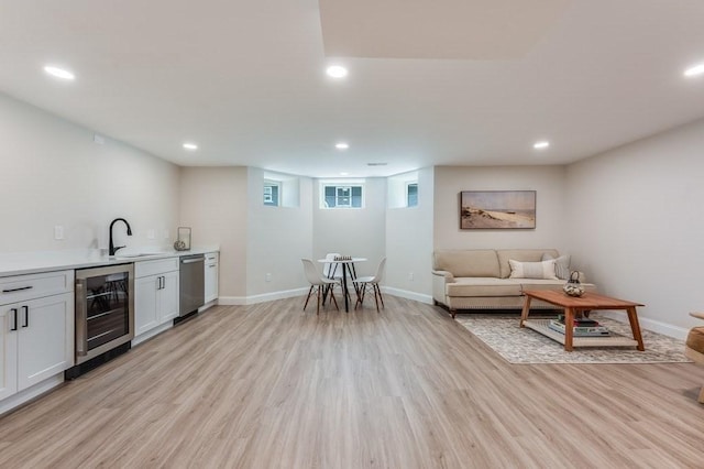 bar featuring wet bar, dishwasher, a sink, light wood finished floors, and beverage cooler