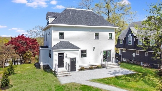 back of property with a shingled roof, a yard, and a patio area