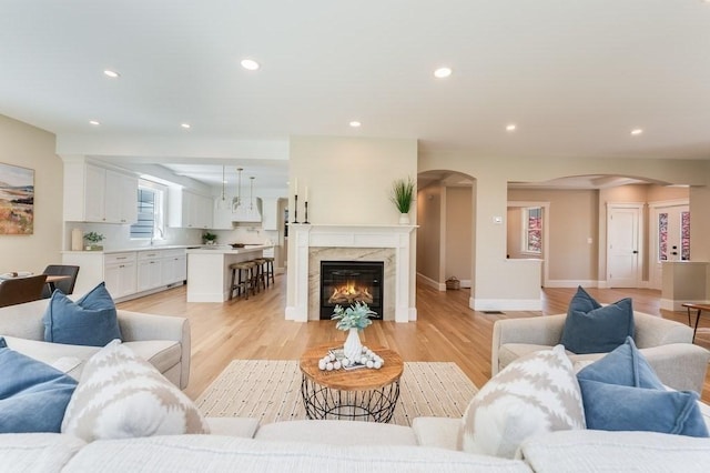living room featuring arched walkways, baseboards, light wood-type flooring, and recessed lighting