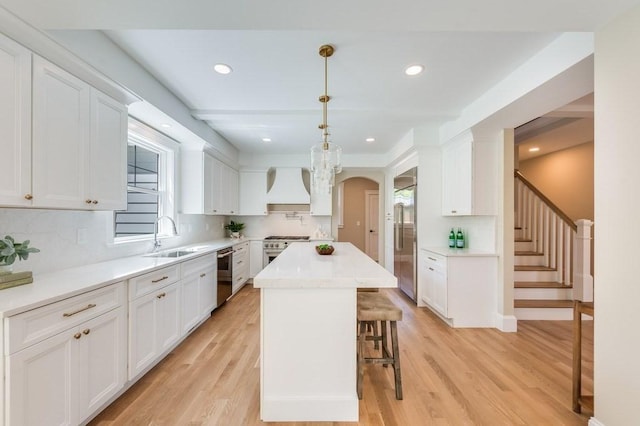 kitchen featuring white cabinets, stainless steel appliances, a sink, and premium range hood