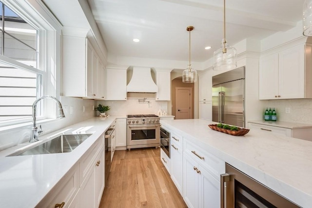 kitchen with high end appliances, premium range hood, recessed lighting, white cabinetry, and a sink