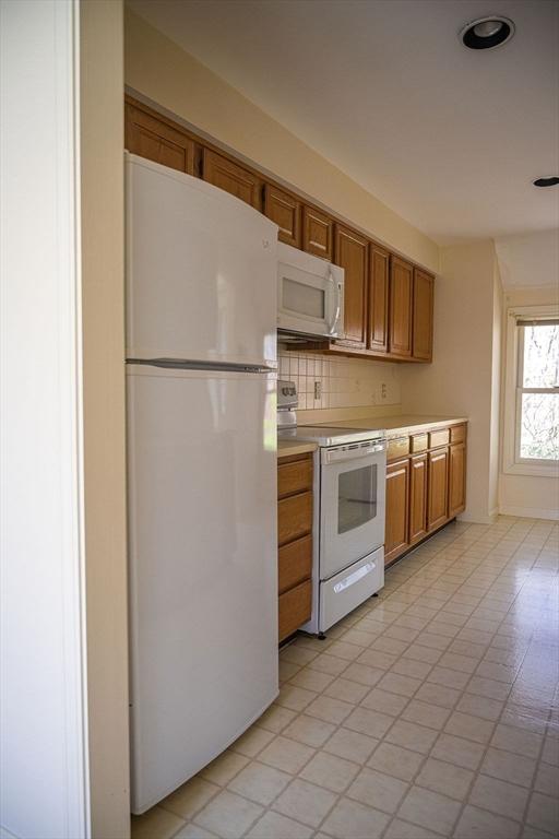 7 Brewster Ln Unit 7, Acton, MA 01720 - kitchen featuring brown cabinetry, white appliances, light countertops, light tile patterned floors, and backsplash
