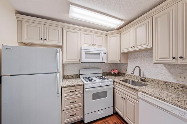kitchen with white appliances, cream cabinetry, and a sink