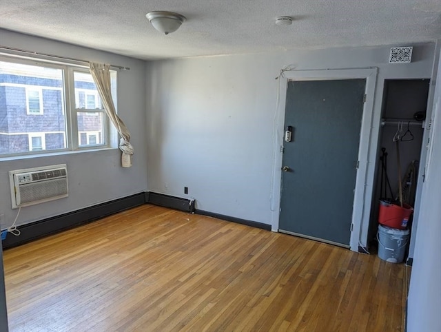 empty room featuring a textured ceiling, light hardwood / wood-style flooring, and a wall mounted AC