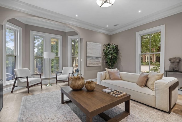 living room featuring crown molding, plenty of natural light, arched walkways, and light wood-type flooring